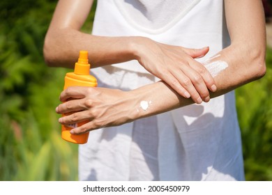 A young girl in a white summer dress applies sunscreen gel to her arms and shoulders, a woman takes care of her skin on a sunny day.