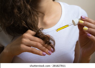 Young girl in a white T-shirt applies her left hand yellow oil on the ends of her curly hair. On her nails bright manicure. Close-up.