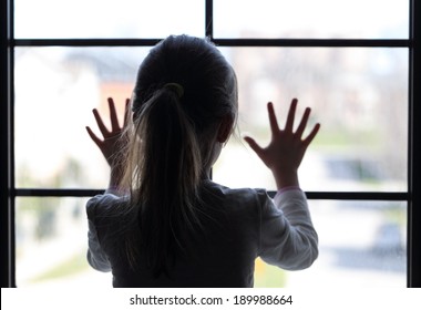 Young girl at window (in partial silhouette) hands pressed against window, pensive or wanting out? 
