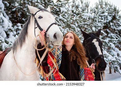 A young girl in winter in the woods stands with horses in the snow