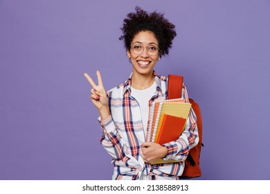 Young girl woman of African American ethnicity teen student in shirt backpack hold books showing victory sign isolated on plain purple background. Education in high school university college concept