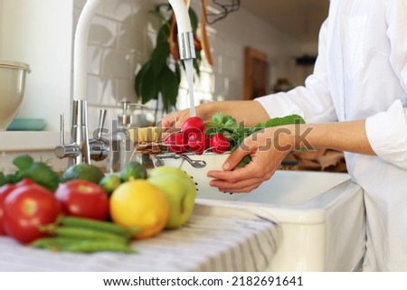 A young girl, a woman, has harvested in the garden, bought at the market, supermarket and washes vegetables and fruits in the kitchen sink. Raw healthy food