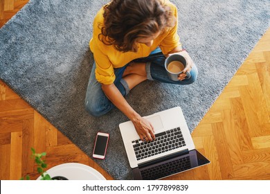 young girl woman in a yellow shirt works on a laptop with a mug of coffee at home in the living room on the carpet, remote work and education - Powered by Shutterstock