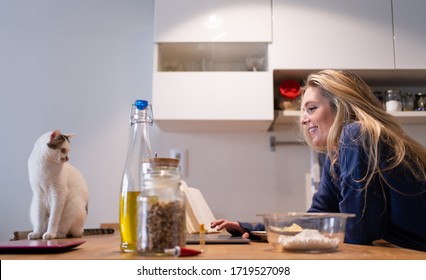 Young Girl Working At The Wooden Kitchen Table Accompanied By Her White Cat And Surrounded By Various Ingredients