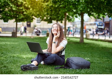 A young girl works with a laptop in the fresh air in the park, sitting on the lawn. The concept of remote work. Work as a freelancer. The girl takes courses on a laptop and smiles. - Shutterstock ID 2160162727