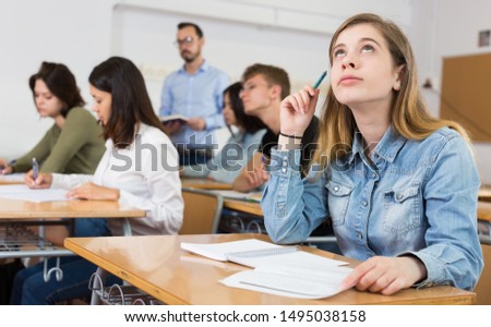 Young girl is writing test and thinking about questions at the desk in the class.