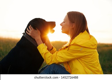  young girl in a yellow raincoat in the summer sunset with a black dog Labrador