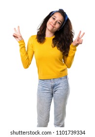 Young girl with yellow sweater and blue bandana on her head smiling and showing victory sign with both hands and with a cheerful face on isolated white background - Shutterstock ID 1101739334