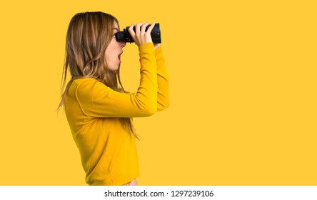 young girl with yellow sweater and looking in the distance with binoculars on isolated yellow background - Shutterstock ID 1297239106