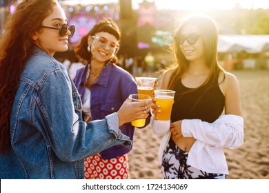Young girlfriends drinking beer and having fun at music festival. Friendship and celebration. Beach party, summer holiday, vacation concept. 