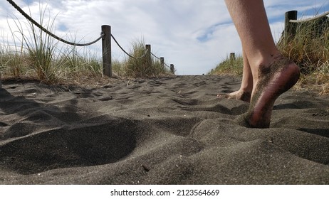A young girl's feet walk on a beach path towards the sea