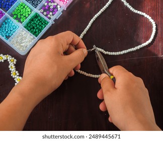 A young girl's hands make a bracelet out of beads, DIY handmade accessories with a bead box kit, and Scissors and pliers , work from home  - Powered by Shutterstock