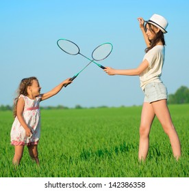 The young girls plays with a racket in badminton over green grass