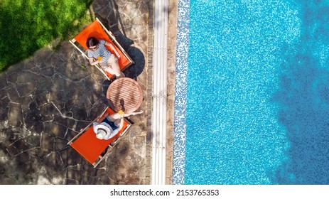 Young Girls Relax Near Swimming Pool In Sunbed Deckchairs, Women Friends Relax On Tropical Vacation In Hotel Resort, Aerial Drone View From Above