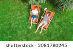 Young girls relax in summer garden in sunbed deckchairs on grass, women friends have fun outdoors in green park on weekend, aerial top view from above