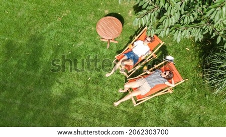 Young girls relax in summer garden in sunbed deckchairs on grass, women friends have fun in green park, aerial top view from above