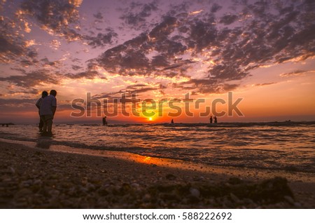 Young girls in warm water at sunset. Gorgeous colors in the sky and the sea. People standing and watching to sunset at Caspian sea. Baku, Azerbaijan. Perfect shapes reflected in water