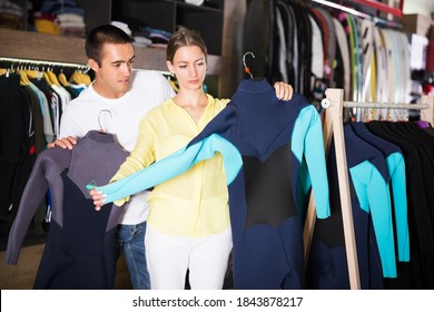 Young Glad Couple Choosing Diving Suit In Clothing Store