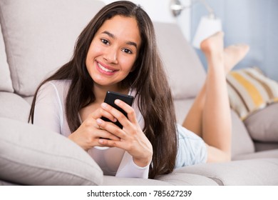 Young glad woman lying on cozy sofa with mobile phone at home - Shutterstock ID 785627239