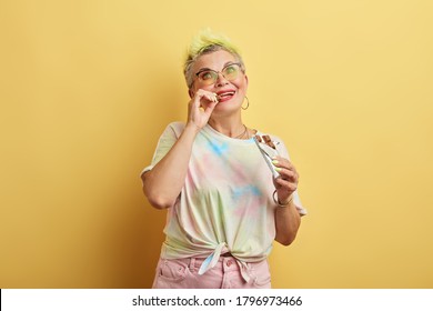 Young Glamour Old Woman Enjoying Eating Chocolate Isolated Over Yellow Wall Background, Old Woman Doesn't Care About Her Weights, Favourite Food, Sweet Tooth, Lifestyle