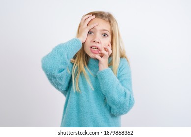 Young Gloomy Cute Caucasian Kid Girl Wearing Blue Knitted Sweater Against White Wall, Hiding Face With Hands Pouting And Crying, Standing Upset And Depressed Complaining About Job Problem.