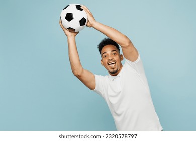 Young goalkeeper happy man fan wear basic t-shirt cheer up support football sport team hold in hand catch soccer ball look camera watch tv live stream isolated on plain pastel blue color background - Powered by Shutterstock