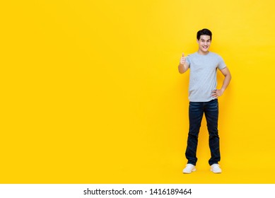 Young Good Looking Asian Man Standing With Thumbs Up Gesture Isolated On Bright Yellow Studio Background With Copy Space