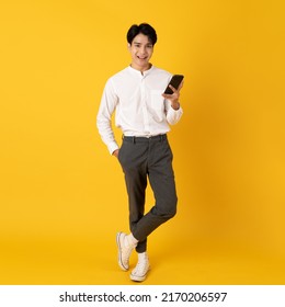 Young Good Looking Asian Man Using Smartphone Isolated On Yellow Background