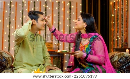 Young good looking brother and sister celebrating Raksha Bandhan or Bhai Dooj festival - Indian Model. Smiling Indian sister putting tika on her brother's forehead with pooja thali 