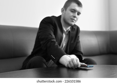 Young Good Looking Male Executive Putting His Mobile Phone On The Table At The Lounge Area. Captured In Gray Scale.