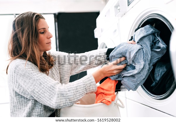 A young and good looking woman is doing\
her laundry in laundromat shop. How to use a washing machine is\
explained in this establishment. Saving time doing house chores is\
essential. Concept:housework