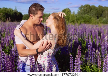 a young gorgeous couple in love tenderly embraces in the morning on a bright blooming lupine field