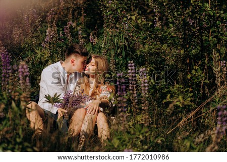 A young gorgeous couple in love tenderly embraces in the morning on a blooming lupine field