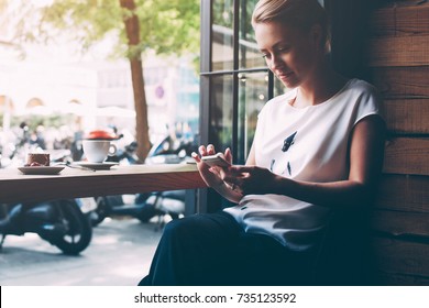 Young gorgeous lady chatting on her smart phone while relaxing in cafe after walking during summer weekend, attractive woman reading text message on cell telephone while sitting in cozy coffee shop - Powered by Shutterstock