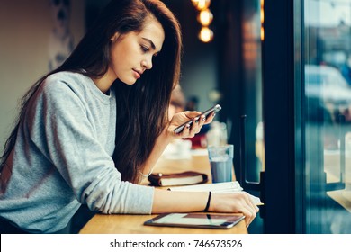 Young gorgeous student checking notification on smartphone connected to wireless internet during browsing information.Charming teenager chatting with followers in social network via telephone