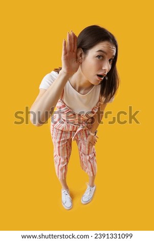 Young gossip woman trying to hear something on yellow background