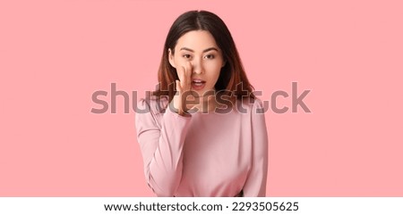 Young gossiping Asian woman on pink background