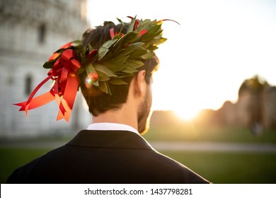 Young Graduate Boy With The Triumphal Laurel Wreath On His Head Seen From Behind.