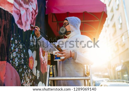 Young graffiti artist painting mural outdoors on street wall.