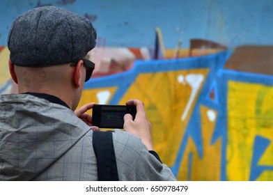 A Young Graffiti Artist Photographs His Completed Picture On The Wall. The Guy Uses Modern Technology To Capture A Colorful Abstract Graffiti Drawing. Focus On The Photographing Device