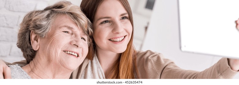 Young granddaughter teaching smiling grandmother how to do selfie with tablet - Powered by Shutterstock