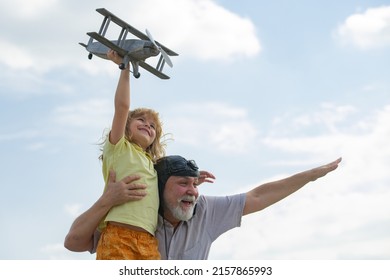 Young Grandson And Old Grandfather Having Fun With Plane Outdoor On Sky Background With Copy Space. Child Dreams Of Flying, Happy Childhood With Grand Dad.