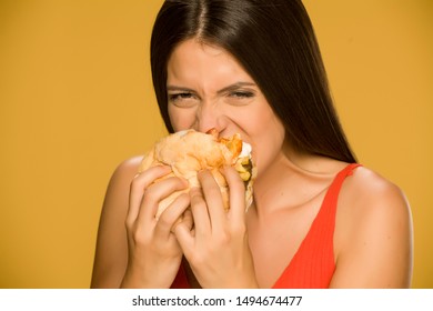 Young Greedy Woman Eating A Burger On Yellow Background