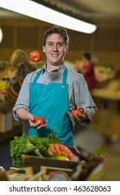 Young Grocery Clerk Juggling With Tomatoes In Produce Aisle Of Grocery Store