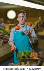 Young Grocery Clerk Juggling With Tomatoes In Produce Aisle Of Grocery Store