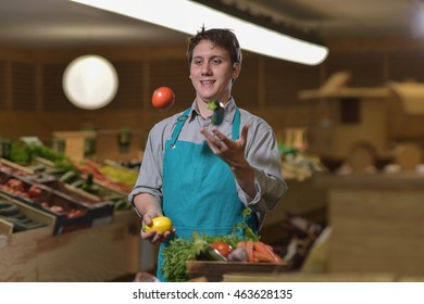 Young Grocery Clerk Juggling With Tomatoes In Produce Aisle Of Grocery Store