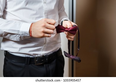 Young groom holding in his hands a red dotted bow-tie. Close-up of men's wedding accessories - Powered by Shutterstock