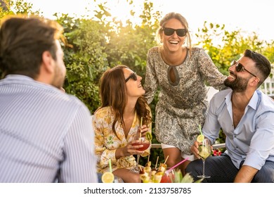 young group of 30s people having fun at a cocktail party outdoor, beautiful women smiling and laughing with friends, handsome men talking with elegant female millenials