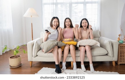 Young group of asian girls friend holding remote control watching TV series show.Beauty cheerful woman teenage sitting on sofa couch having fun relax leisure time at home. Stay home activities. - Powered by Shutterstock