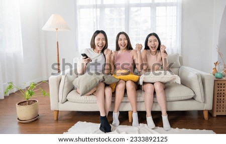 Young group of asian girls friend holding remote control watching TV series show.Beauty cheerful woman teenage sitting on sofa couch having fun relax leisure time at home. Stay home activities.